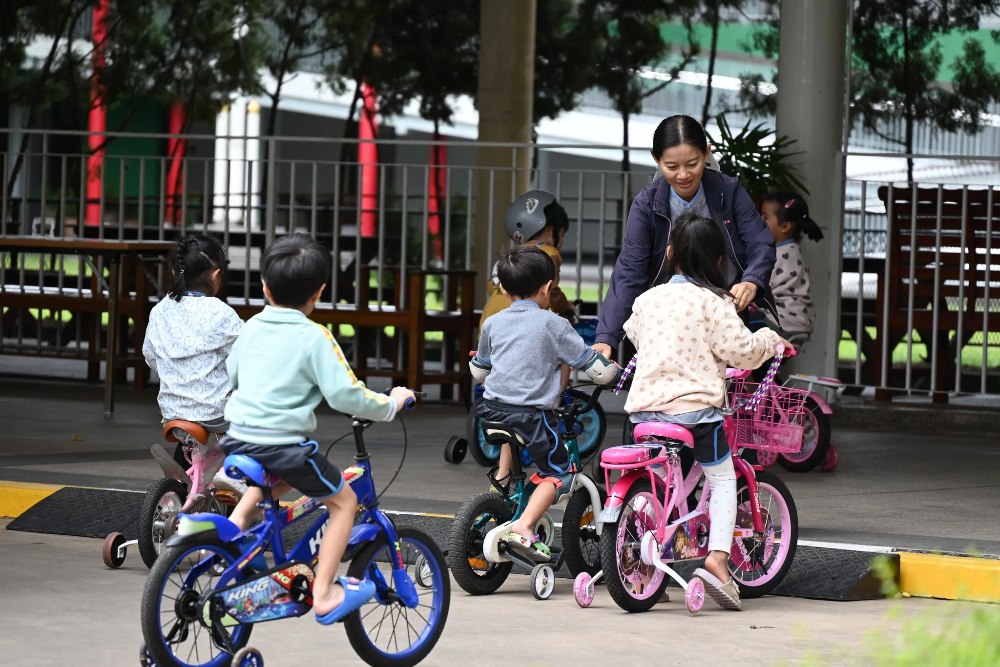 เด็กๆ ขี่จักรยานในพื้นที่เล่นกลางแจ้งพร้อมครูช่วยเหลือ